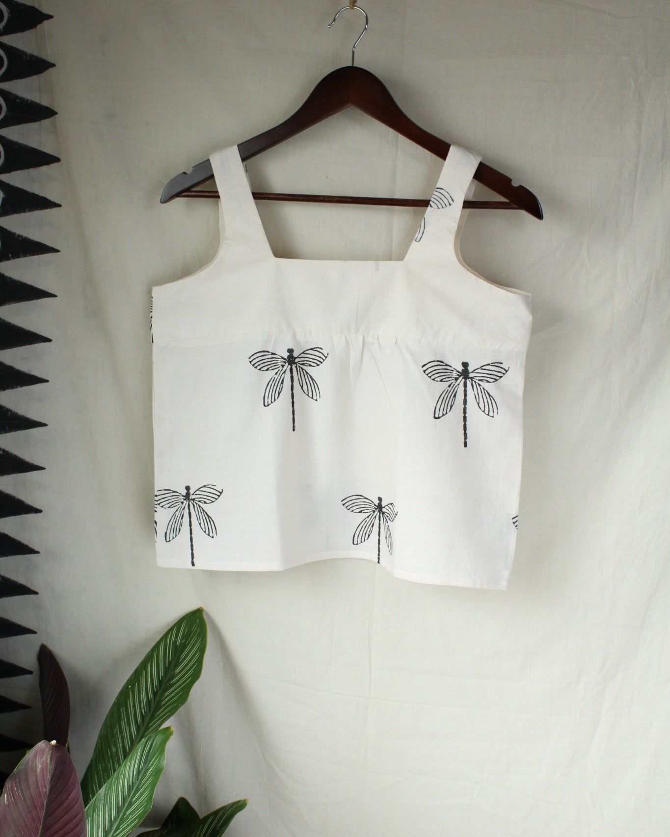 White tank top with black dragonfly designs on a hanger against a white background